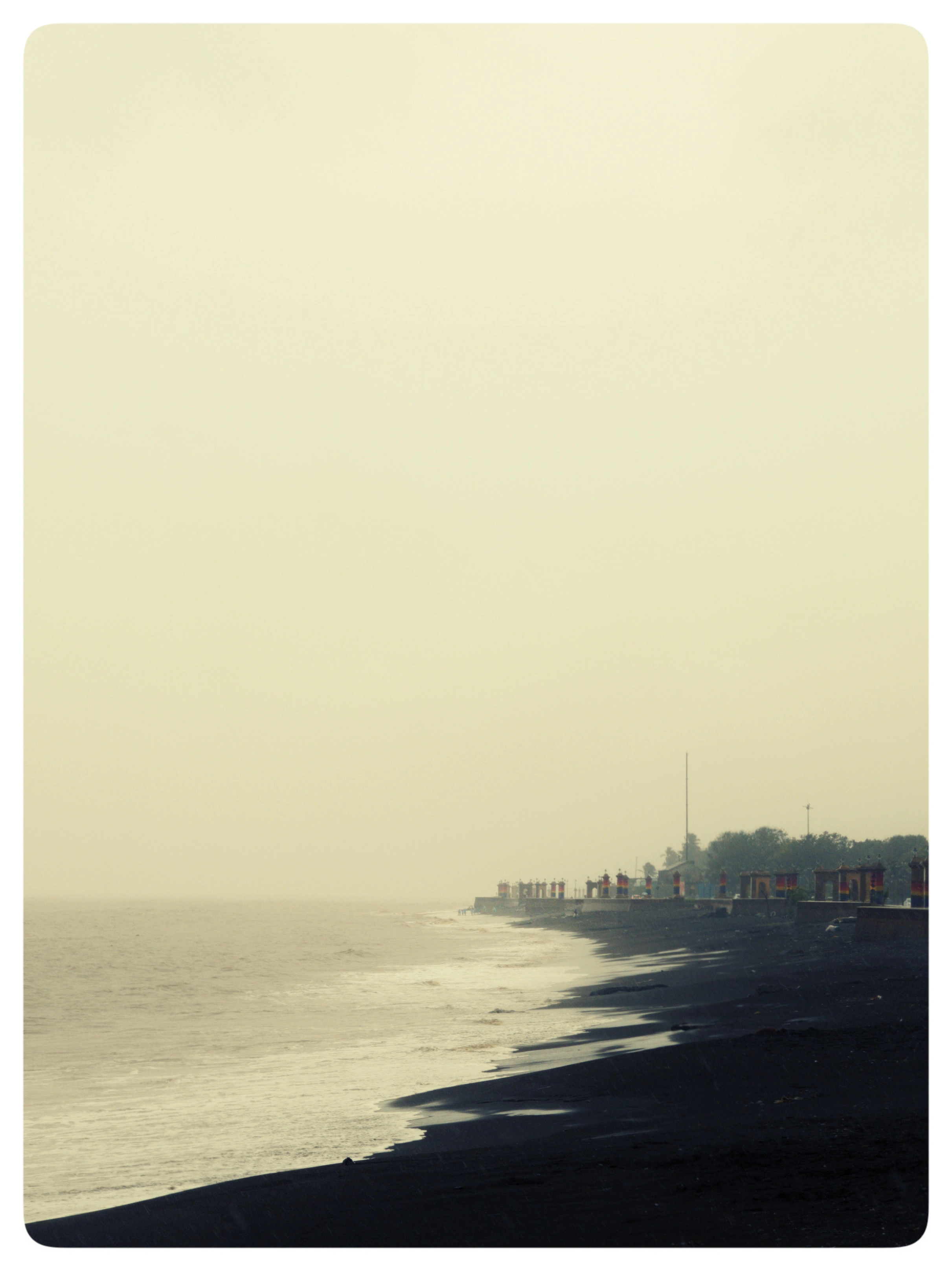 A pale sea meets a dark curved shoreline beneath a hazy sky.