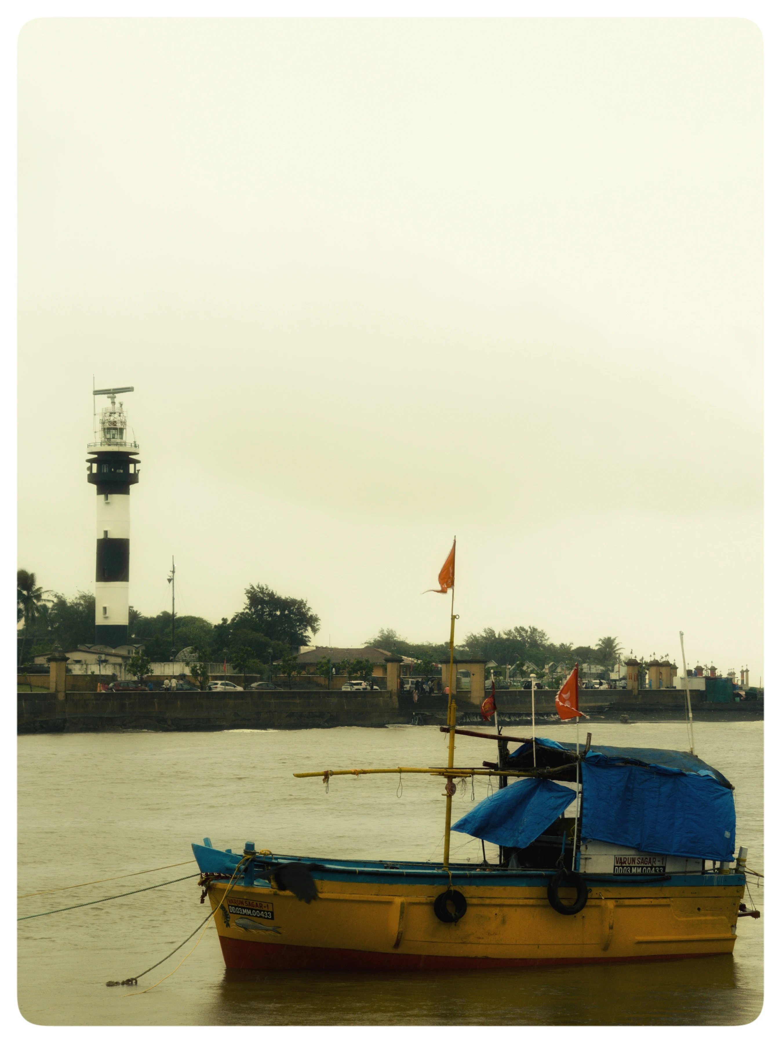 A yellow boat with a blue canopy floats near a harbour and a distant tower.