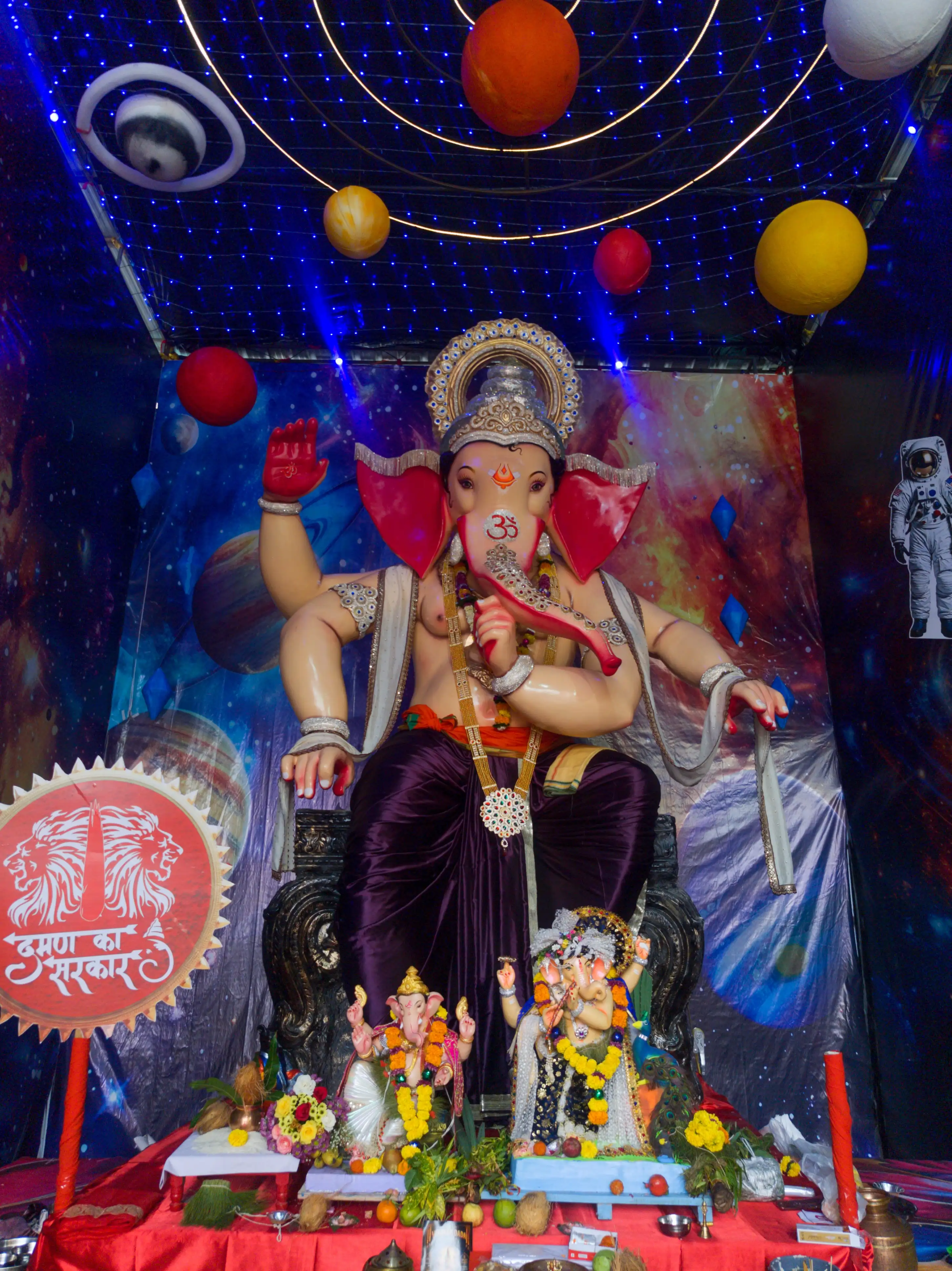 A Ganesha idol displayed against a deep-blue backdrop with colourful planet decorations.