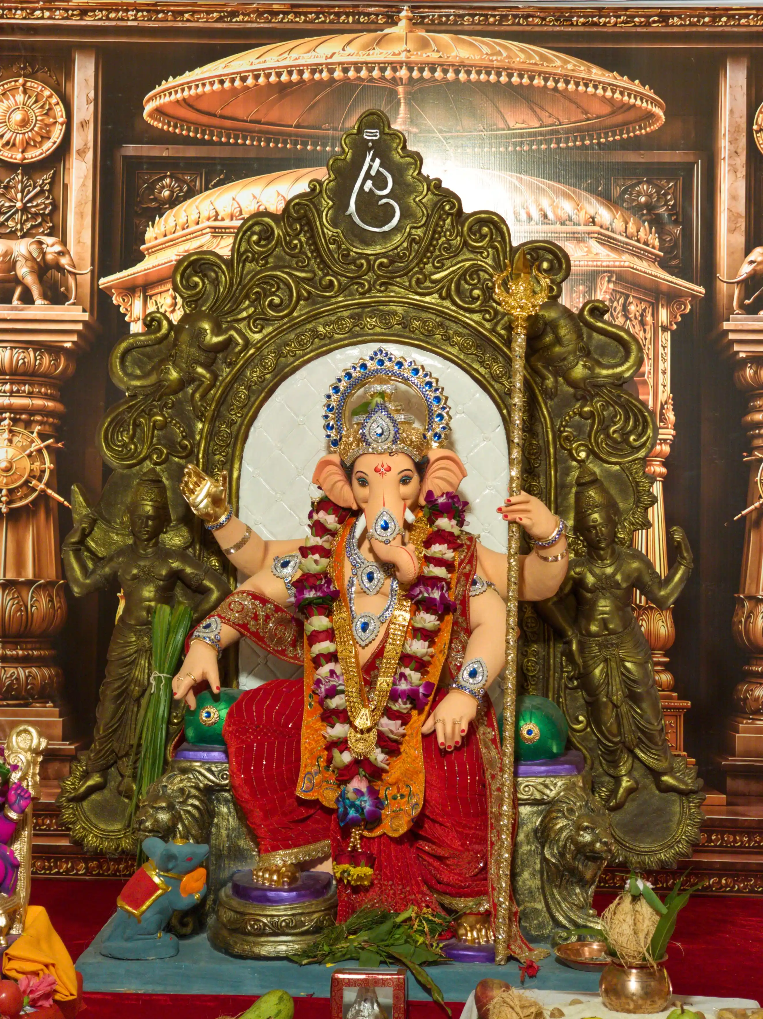 A Ganesha idol covered in flower garlands sits beneath a large golden arch.