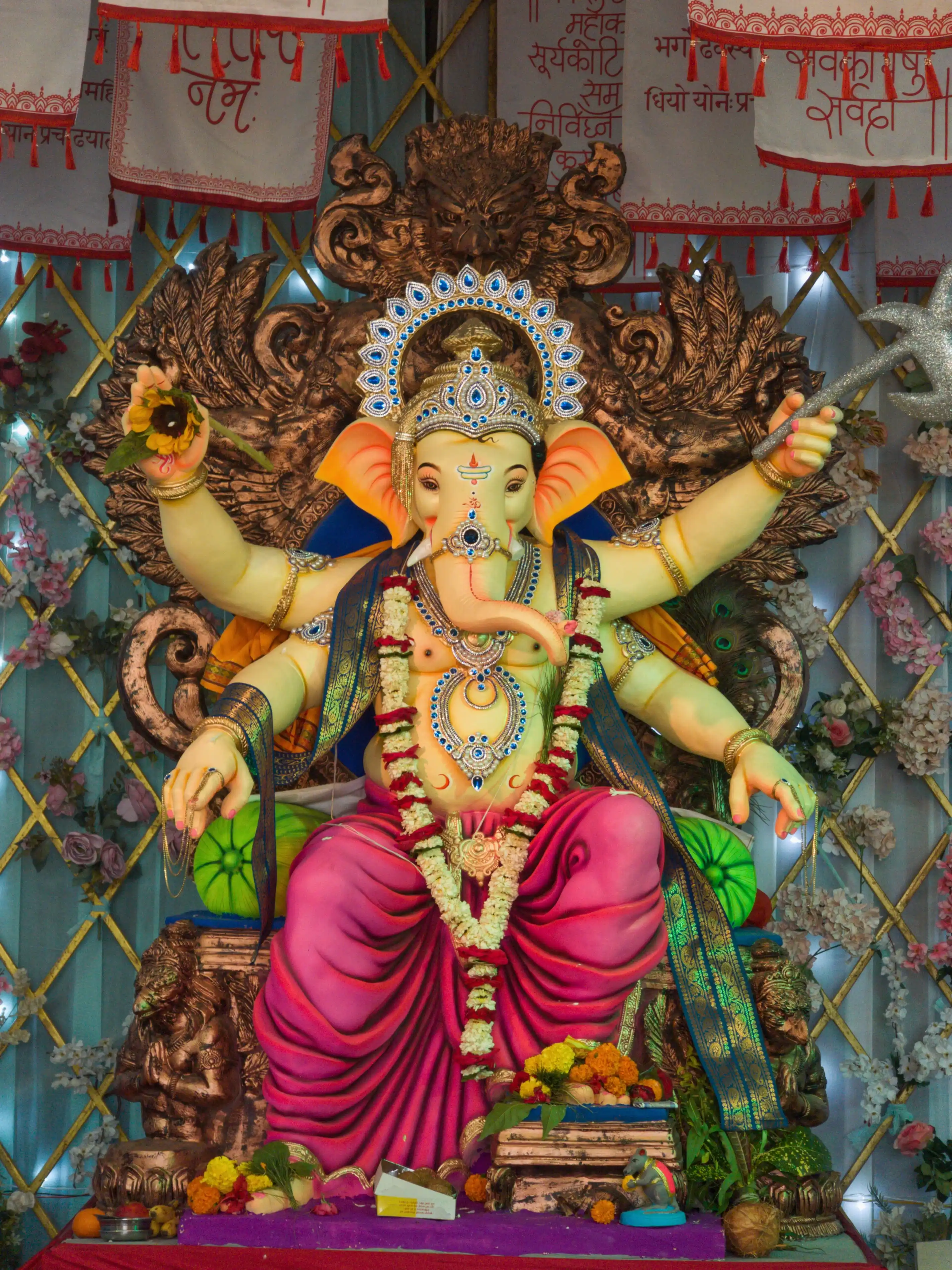 A Ganesha idol in a bright pink dhoti sits beneath an elaborate decorative arch.