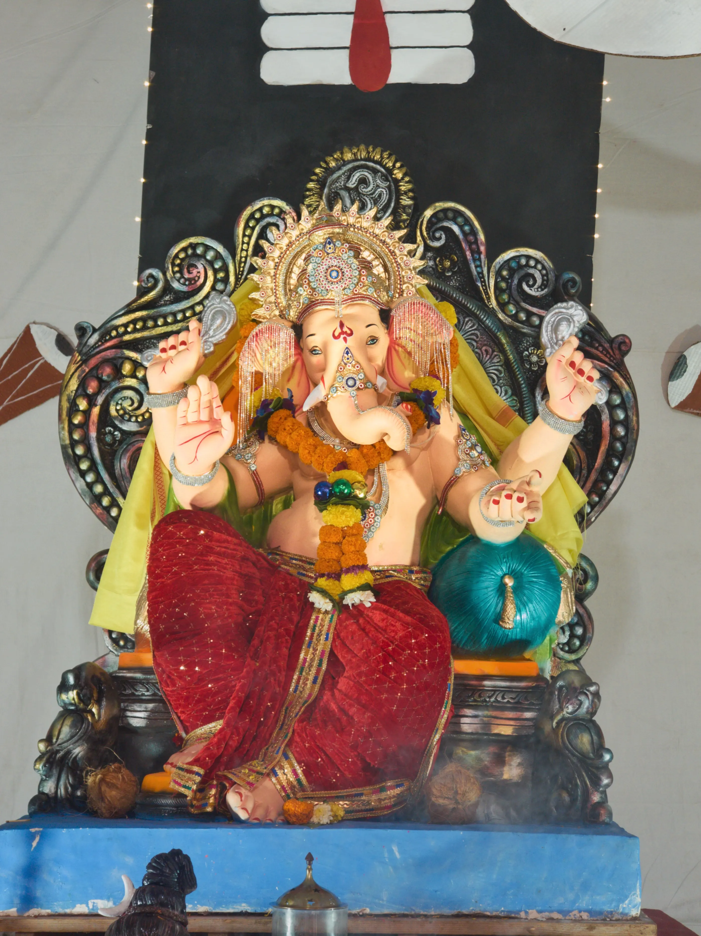 A Ganesha idol wearing red fabric sits on an ornate gold-and-blue throne.
