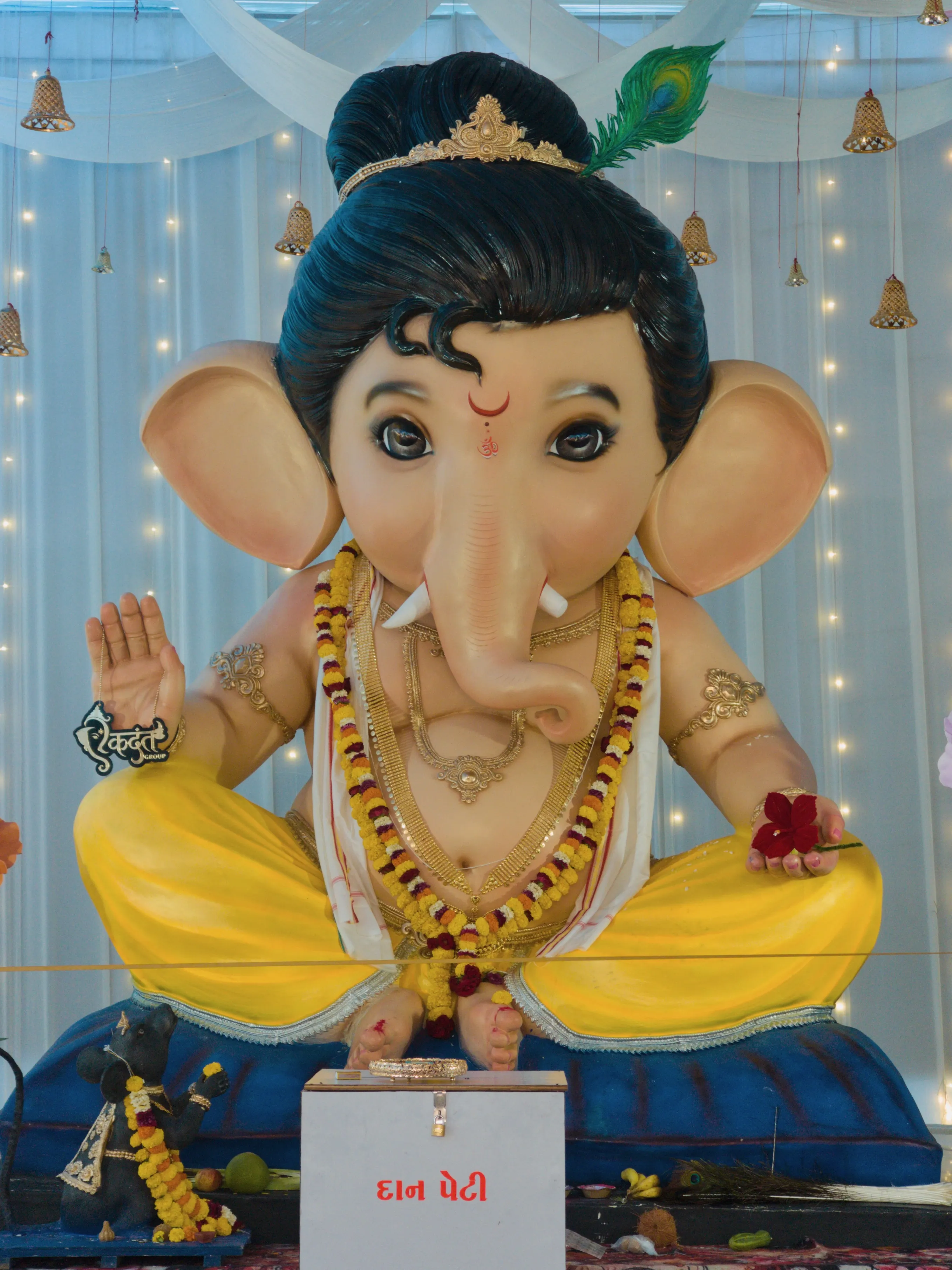 A close view of a Ganesha idol in yellow clothing against a pale-blue backdrop.