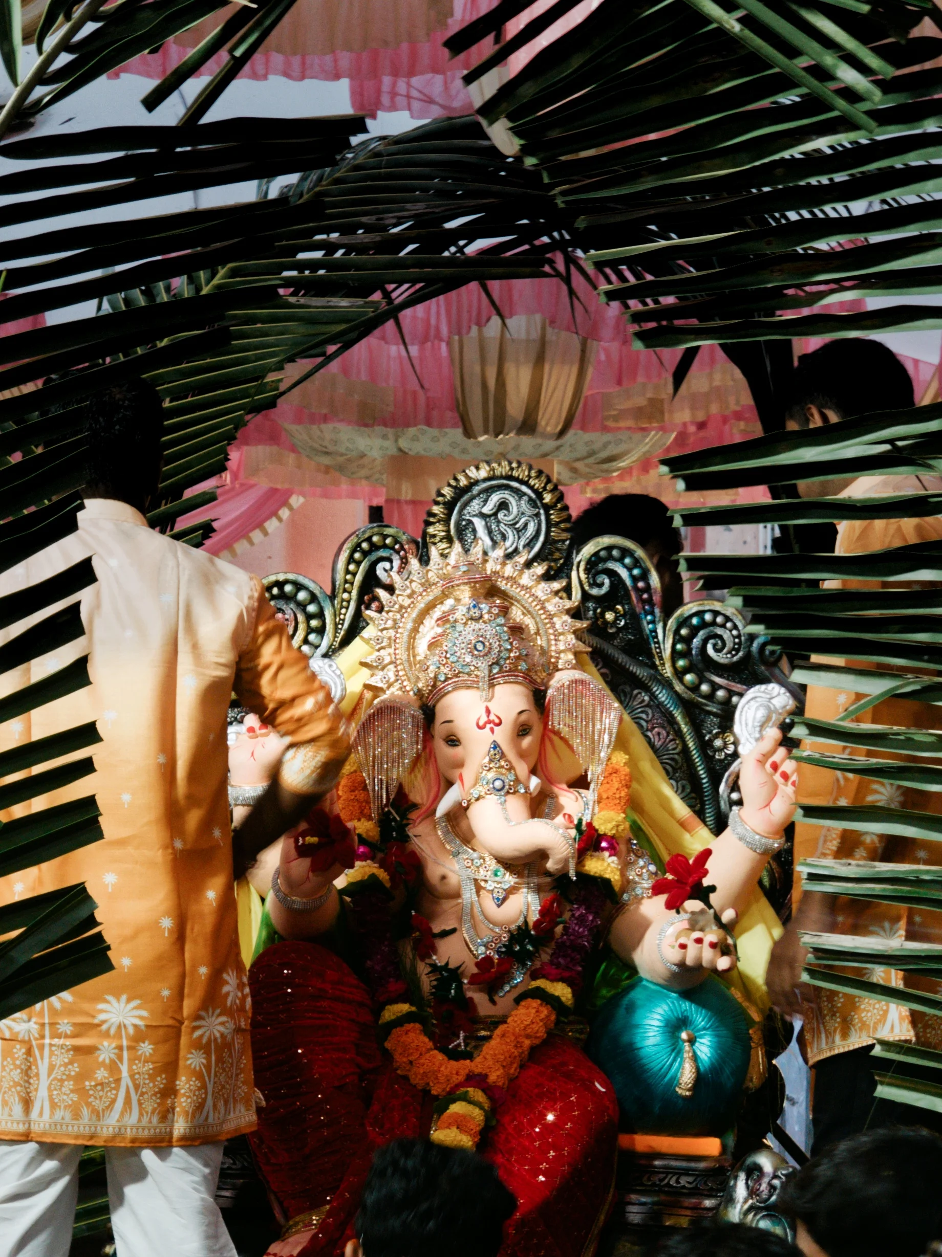 A decorated Ganesha shrine beneath a canopy of long dark-green leaves.