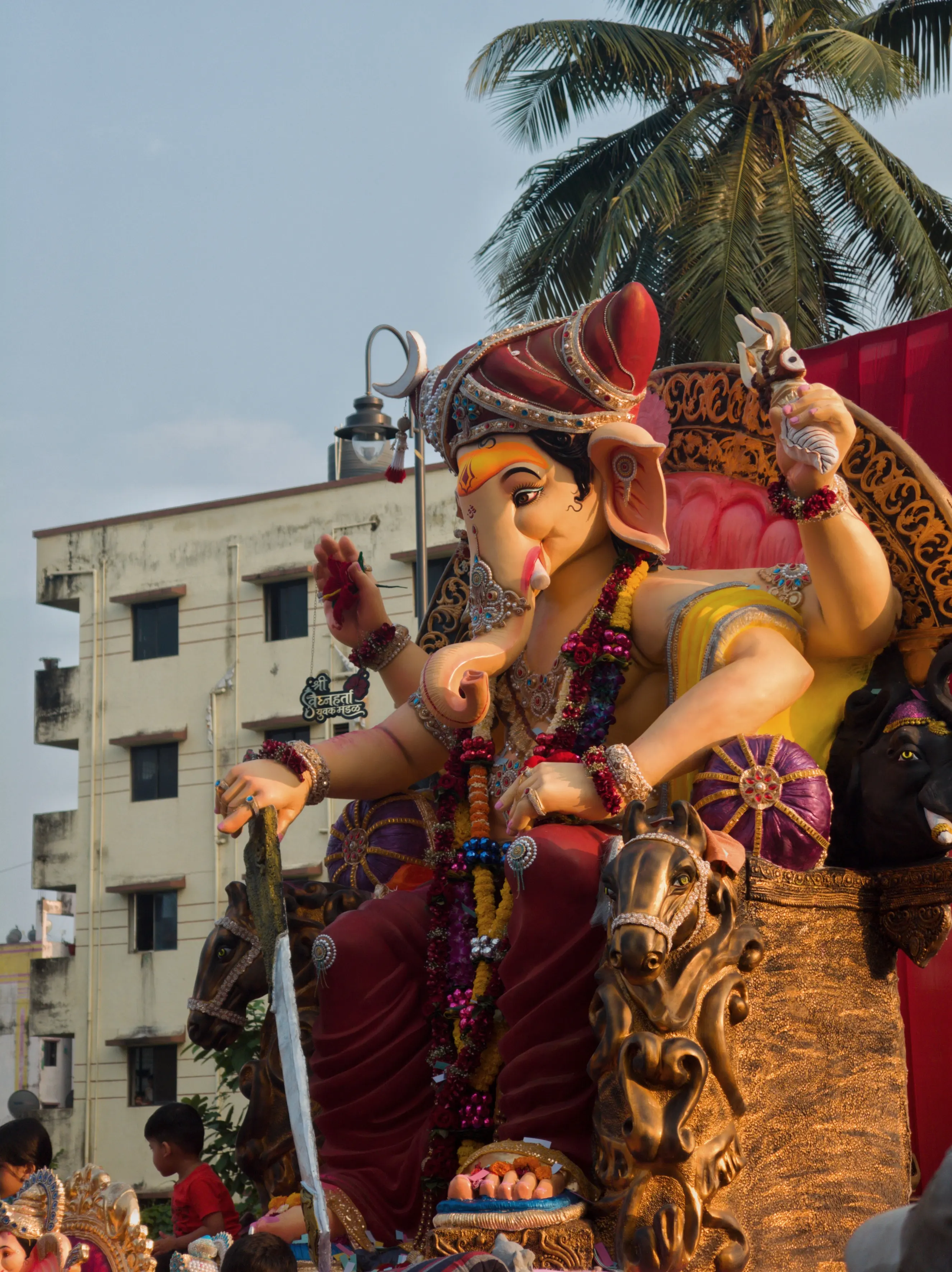 An outdoor Ganesha display with decorative arches, a palm tree and nearby buildings.
