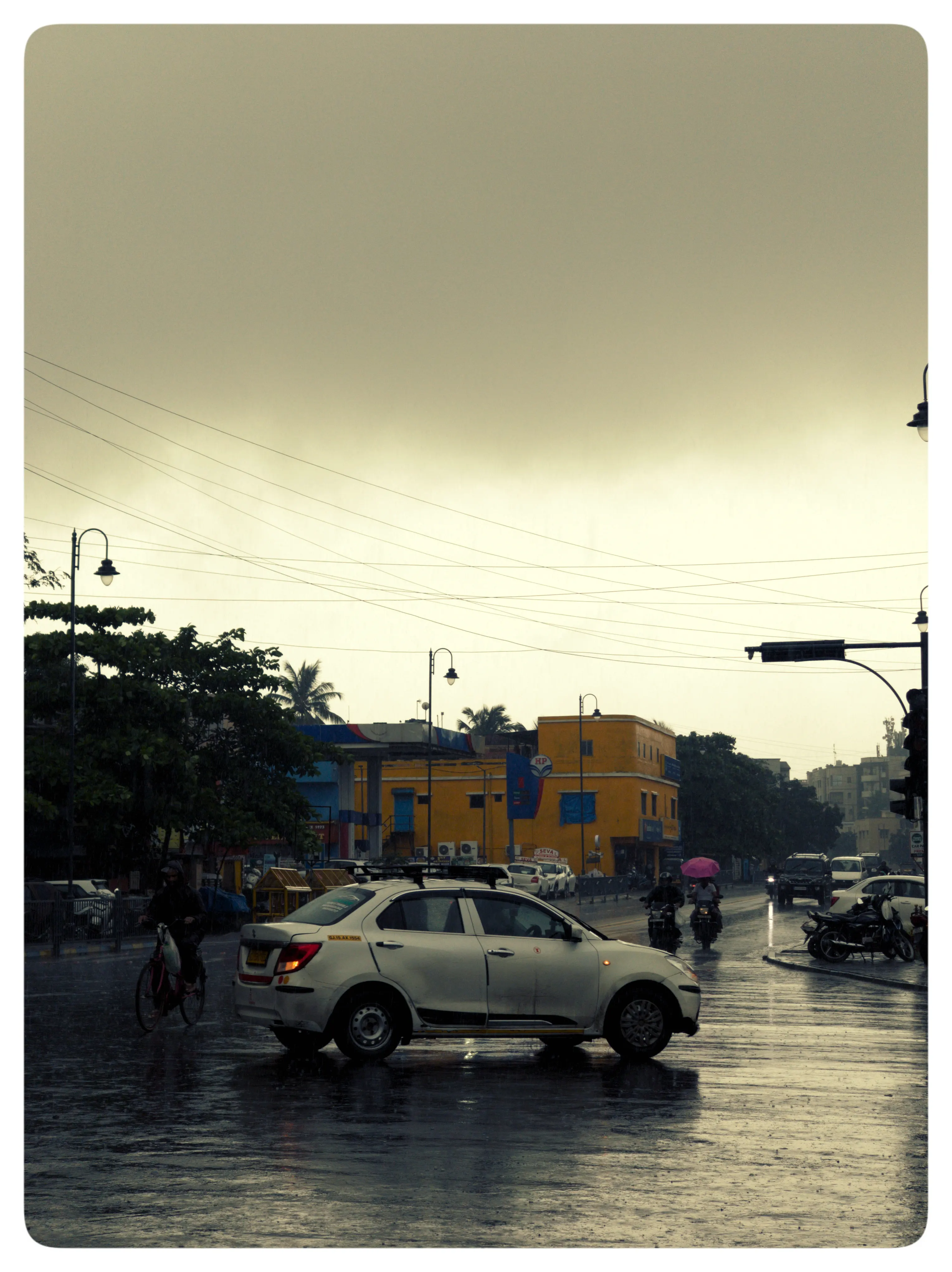 A silver car crosses a rain-darkened intersection beneath an overcast sky.